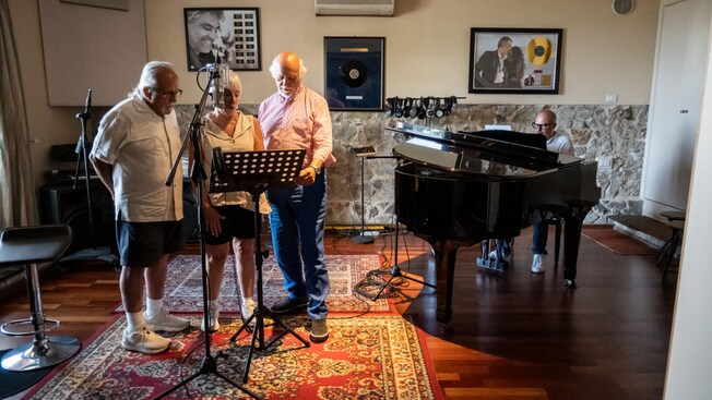 Three Guests singing in front of a microphone while music producer Pierpaolo Guerrini plays a grand piano