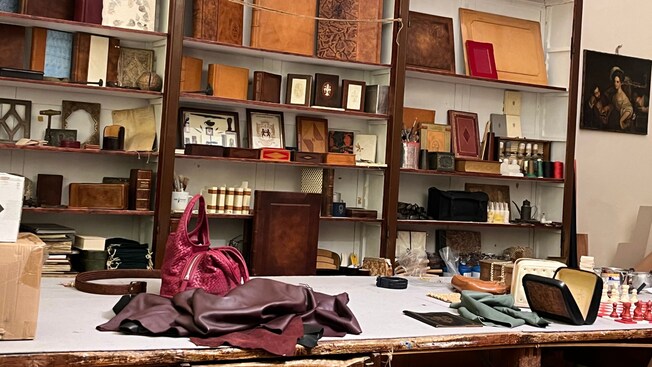 Estantes de madera llenos de libros encuadernados con cuero, herramientas y suministros de manualidades, y una mesa con materiales de cuero