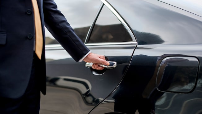 A private driver opening the door of a luxury sedan A private driver opening the door of a luxury sedan