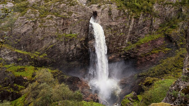 A large waterfall pouring through a rock face onto a valley below