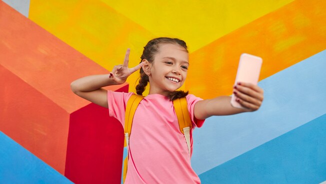 A young girl taking a selfie in front of a mural