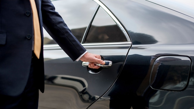 A private driver opening the door of a luxury sedan A private driver opening the door of a luxury sedan