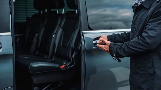 A private driver opening the door of a luxury minibus A private driver opening the door of a luxury minibus