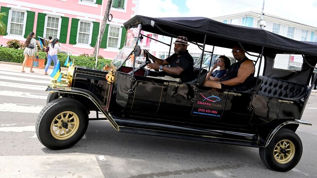 A couple being driven on a tour in a vintage wagon style car