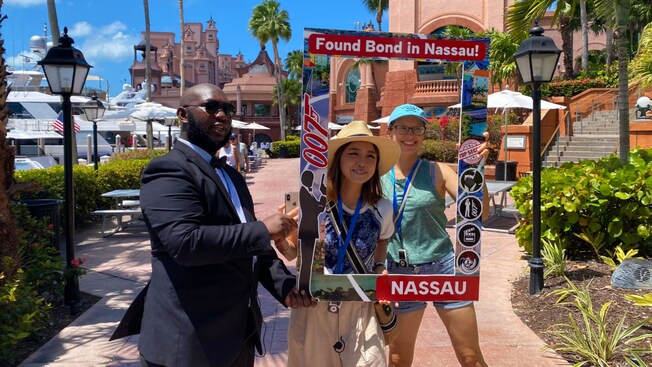 2 visitors pose for a picture on Nassau with a sign that reads ‘Found Bond in Nassau’
