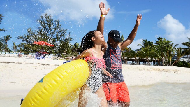 2 Guests holding a water raft splashing in the ocean along Blue Lagoon Island
