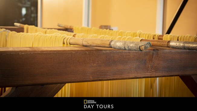 Pasta noodles drying on wooden racks, with text below that says, 'National Geographic Day Tours'