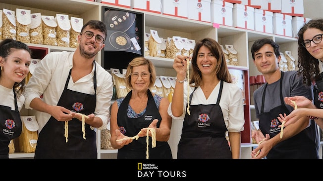 Un instructor y estudiantes sosteniendo la pasta que elaboraron, con un texto debajo que dice “National Geographic Day Tours” Un instructor y estudiantes sosteniendo la pasta que elaboraron, con un texto debajo que dice “National Geographic Day Tours”