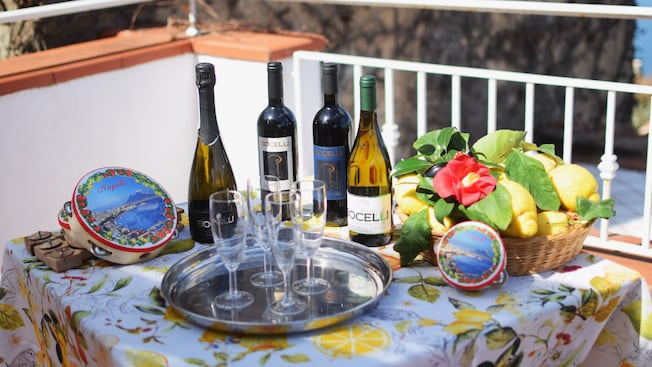 Table set with wine bottles, a tray of glasses, a basket of lemons and decorative tins on a lemon themed tablecloth Table set with wine bottles, a tray of glasses, a basket of lemons and decorative tins on a lemon themed tablecloth