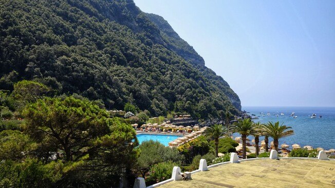 A thermal pool, lying between a forested hillside and the ocean