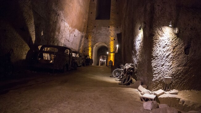 A dark tunnel with dirt, cars and a bike in the Galleria Borbonica in Naples, Italy