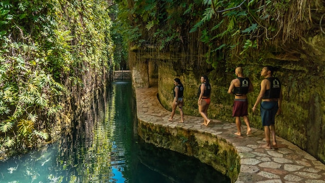A group of people walking on a path next to a body of water in an open air cave in Progreso, Mexico A group of people walking on a path next to a body of water in an open air cave in Progreso, Mexico