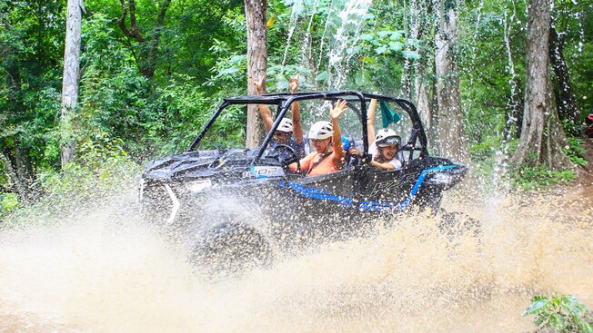 Guests in an off road vehicle driving through a muddy area