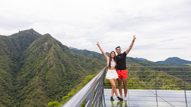 A man and woman posing on an observation deck with mountains in the background