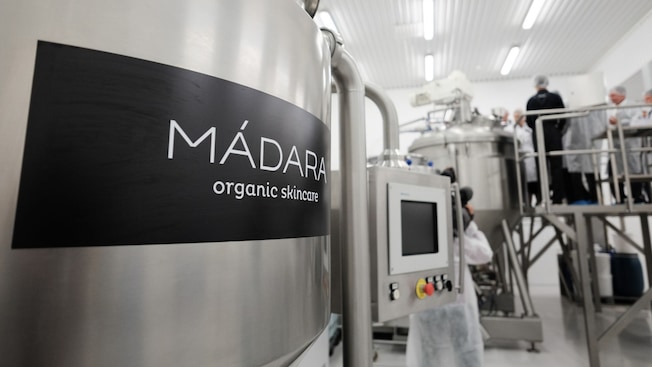 A large stainless steel tank with the words Madara Organic Skincare next to workers attending another nearby tank A large stainless steel tank with the words Madara Organic Skincare next to workers attending another nearby tank