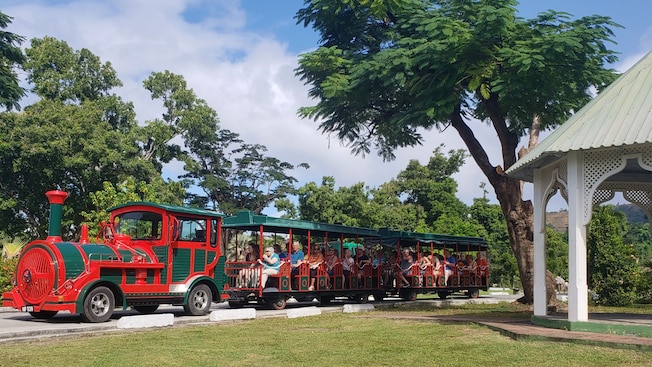 Um bonde cheio de passageiros parado em uma área arborizada junto a um gazebo. Um bonde cheio de passageiros parado em uma área arborizada junto a um gazebo.