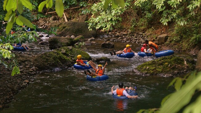 A group of people in inflatable tubes, life vests and helmets rafting down a river