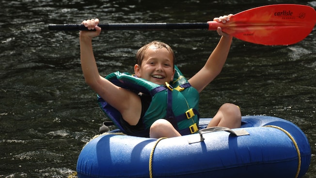 Um menino em um bote inflável no Wacky River, em Dominica, segurando um remo acima da cabeça Um menino em um bote inflável no Wacky River, em Dominica, segurando um remo acima da cabeça
