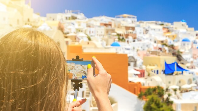 A woman photographing houses in Santorini on her smart phone using a selfie stick
