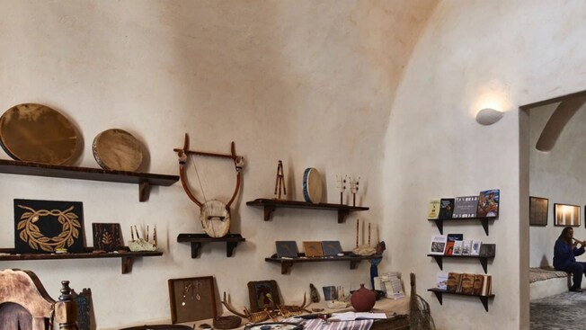 Uma sala exibindo instrumentos musicais da Grécia Antiga e um homem tocando flauta doce em uma sala adjacente