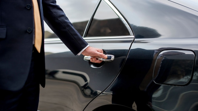 A private driver opening the door of a luxury sedan A private driver opening the door of a luxury sedan