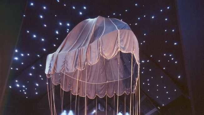 Un antiguo paracaídas colgando en una exhibición con estrellas proyectadas en la pared y el techo Un antiguo paracaídas colgando en una exhibición con estrellas proyectadas en la pared y el techo