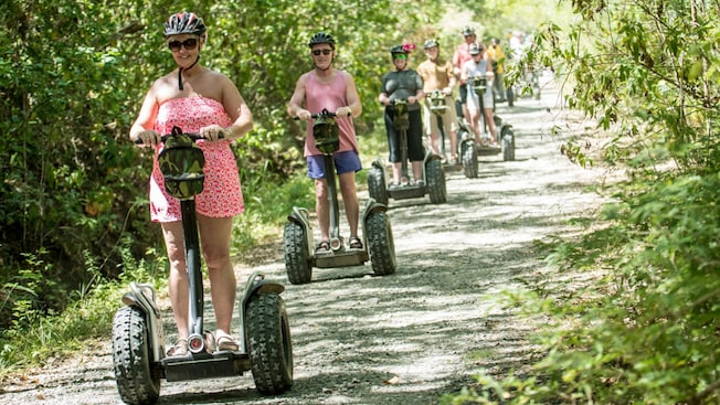 Guests wearing helmets on Segways lined up on a trail Guests wearing helmets on Segways lined up on a trail