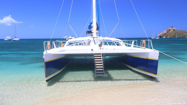 Un catamarán de navegación atracado en la playa con otros botes en el agua a la distancia