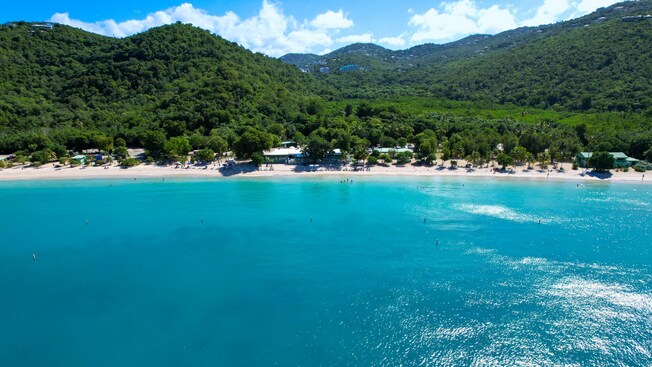 A tropical beach in Saint Thomas with a serene sea and some small buildings on the sandy shore