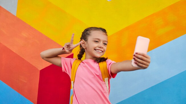 A girl taking a selfie in front of a bright, multicolored wall