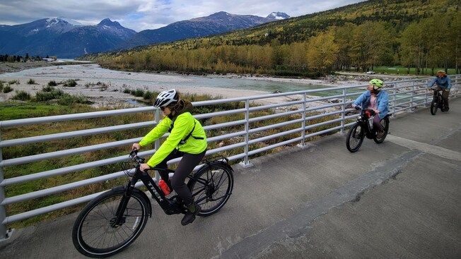Três pessoas andando de bicicleta em uma ponte sobre um rio no Alasca