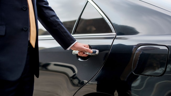 A private driver opening the door of a luxury sedan A private driver opening the door of a luxury sedan