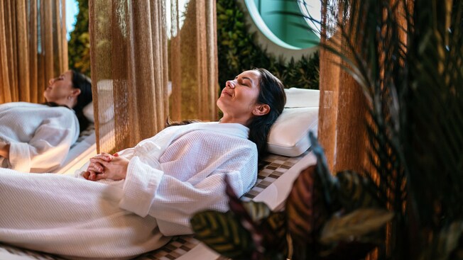 Two women relaxing on cushioned lounge chairs inside a spa