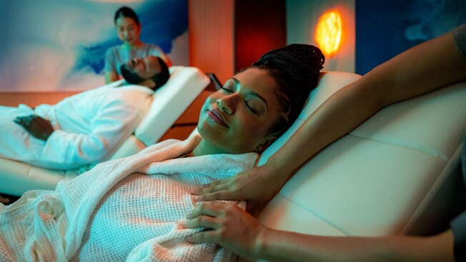A man and a woman with their eyes closed getting a massage on reclining massage chairs