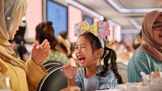 Una niña se ríe con su familia mientras disfruta de una comida en Animator’s Table en el crucero Disney Adventure Una niña se ríe con su familia mientras disfruta de una comida en Animator’s Table en el crucero Disney Adventure