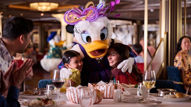 Daisy Duck hugging 2 Guests while they dine with their family at Navigator’s Club on the Disney Adventure cruise ship Daisy Duck hugging 2 Guests while they dine with their family at Navigator’s Club on the Disney Adventure cruise ship