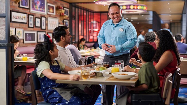 Un Miembro del Elenco conversando con los Huéspedes mientras cenan en Pixar Market Restaurant en el crucero Disney Adventure