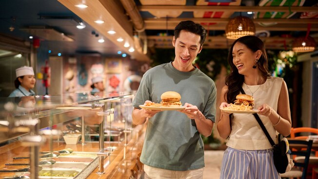 Dos Huéspedes sosteniendo sus platos con sándwiches y papas fritas de Stitch’s Ohana Grill en el crucero Disney Adventure