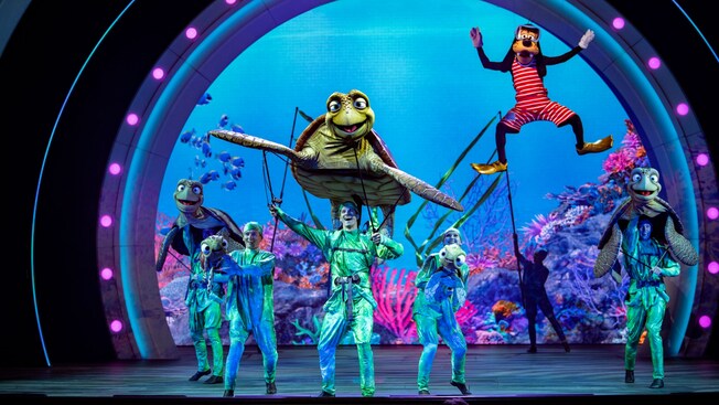 Goofy y Crush con un grupo de artistas en el escenario durante un espectáculo de Disney Seas the Adventure