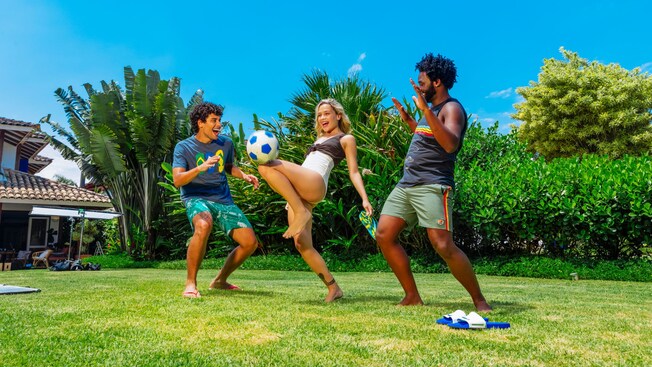 Three friends play outside as a girl kicks a soccer ball with her knee