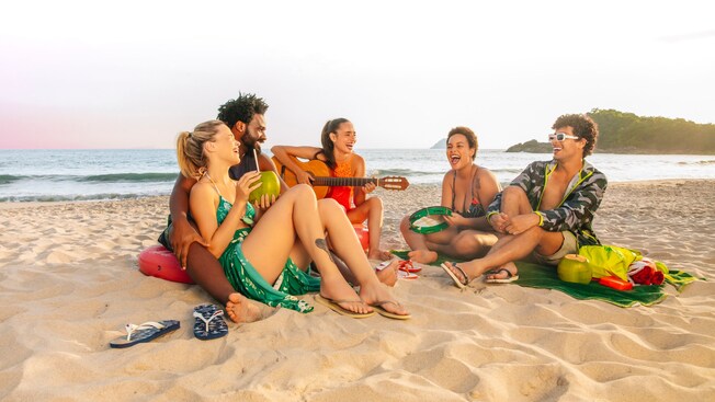 A group of friends sit in a circle on the beach, talking and laughing