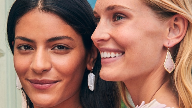 2 smiling women wearing dangly earrings featuring large gemstones