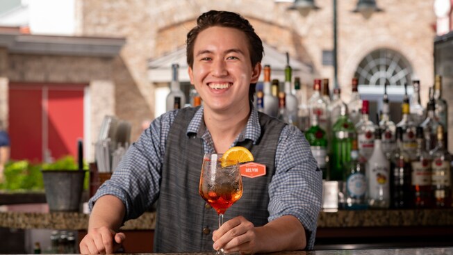 A smiling bartender holding a beverage at an outside bar