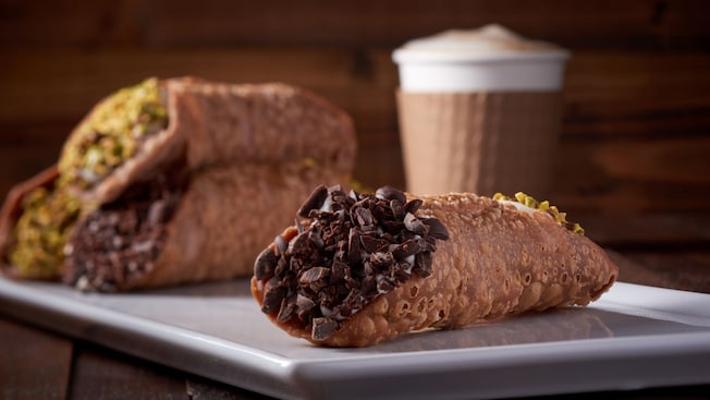 Quatro cannolis servidos em um prato perto de um café