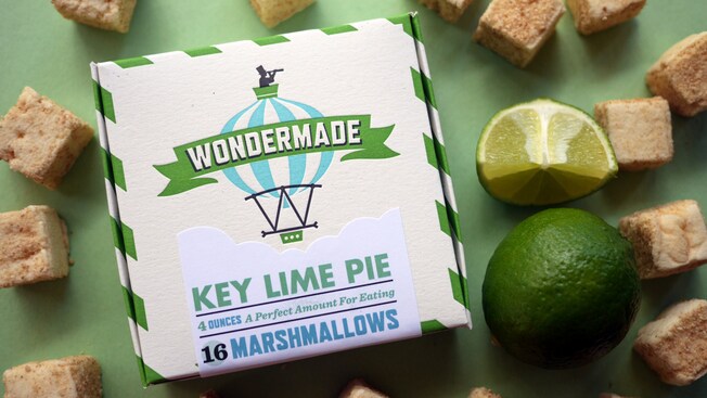 A box of 16 Key Lime Pie flavored Wondermade marshmallows, surrounded by a sliced lime, and marshmallow squares topped with graham cracker crumbs.