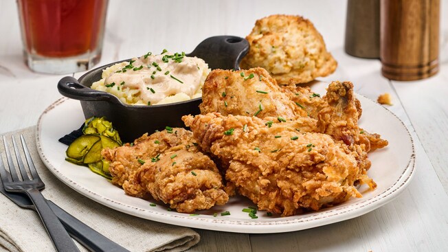 A fried chicken dinner platter with mashed potatoes and a biscuit