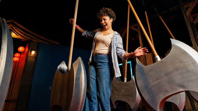 A young woman laughing while navigating between large swinging axe like pendulums in a darkened challenge room