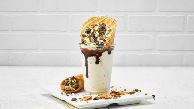 Um Cannolli Shake com chantili, pistache, pedaços de chocolate e um cone de waffle