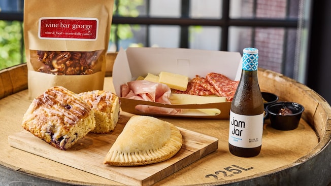 Queijo fatiado, embutidos e doces ao lado de uma sacola com um rótulo no qual se lê Wine Bar George, vinho e comida magistralmente harmonizados, em inglês