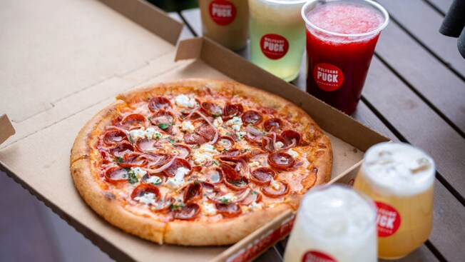 A pizza in a box next to several beverages